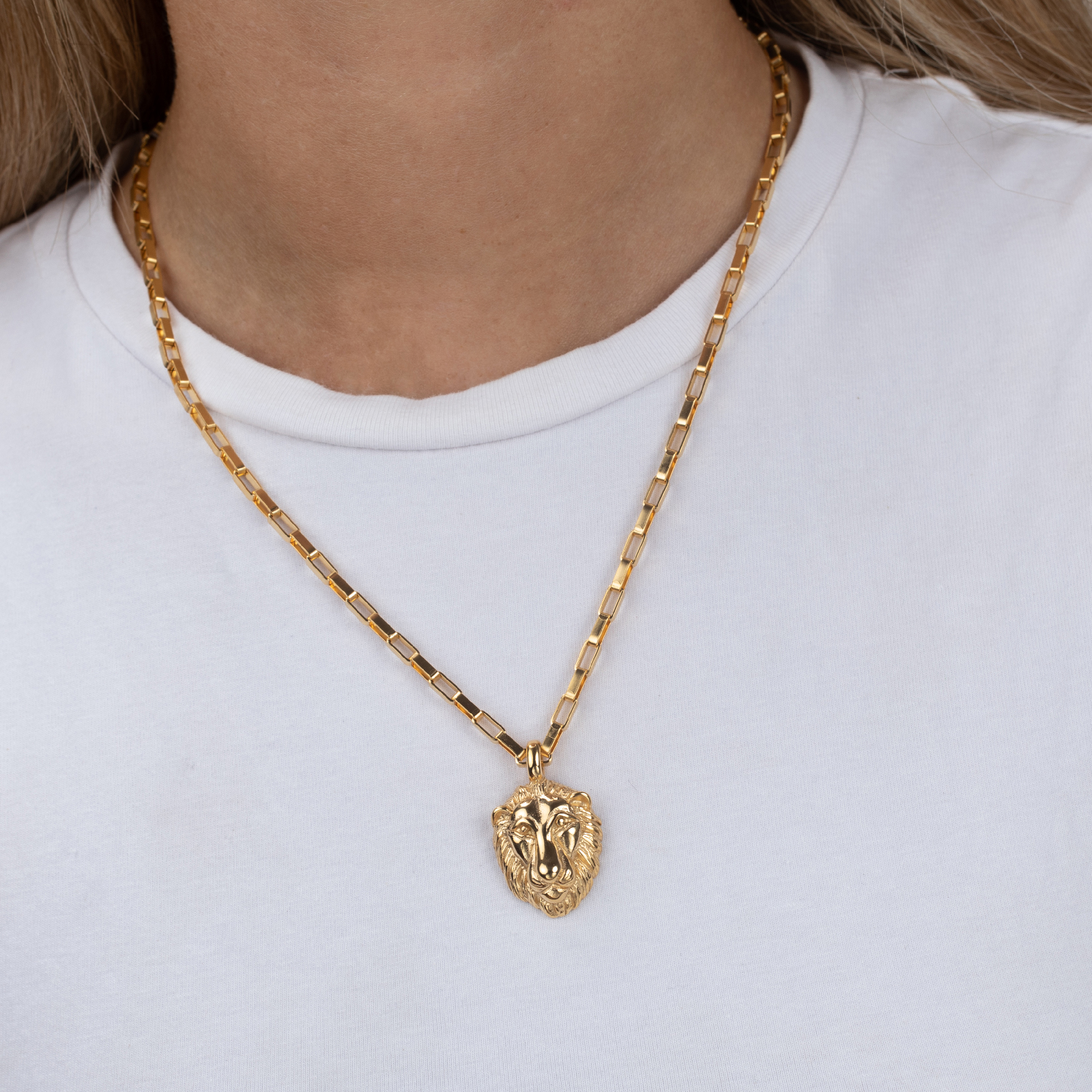 Colar dourado com pendente de cabeça de leão numa pessoa com t-shirt branca