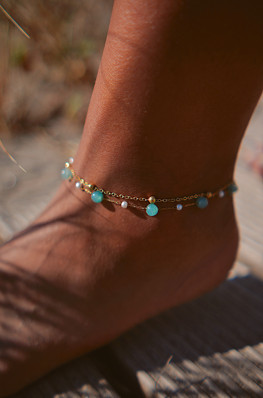 Tornozeleira dourada com pedras azuis e brancas no tornozelo