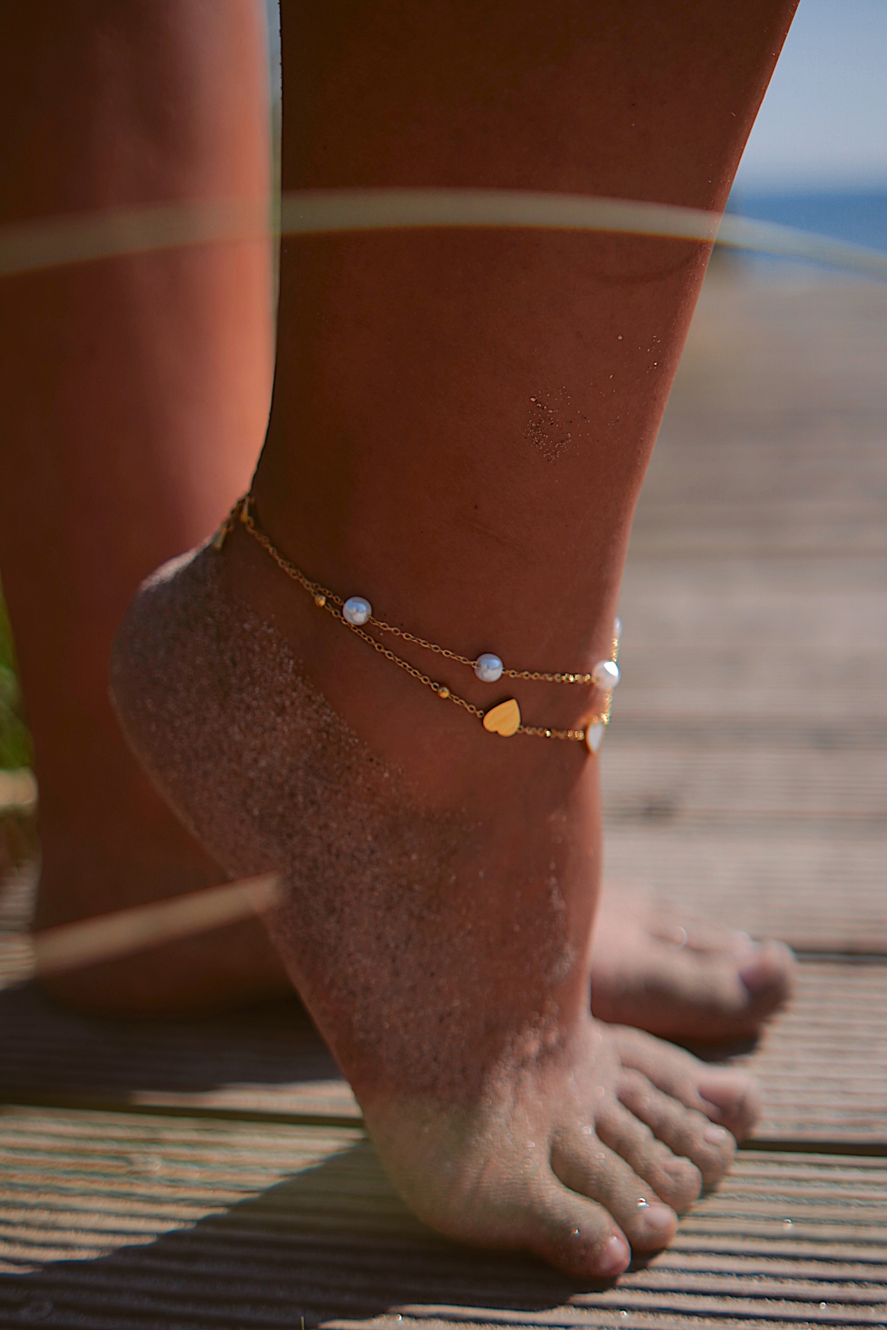 Pé com tornozeleira dourada com contas brancas e coração amarelo ao ar livre