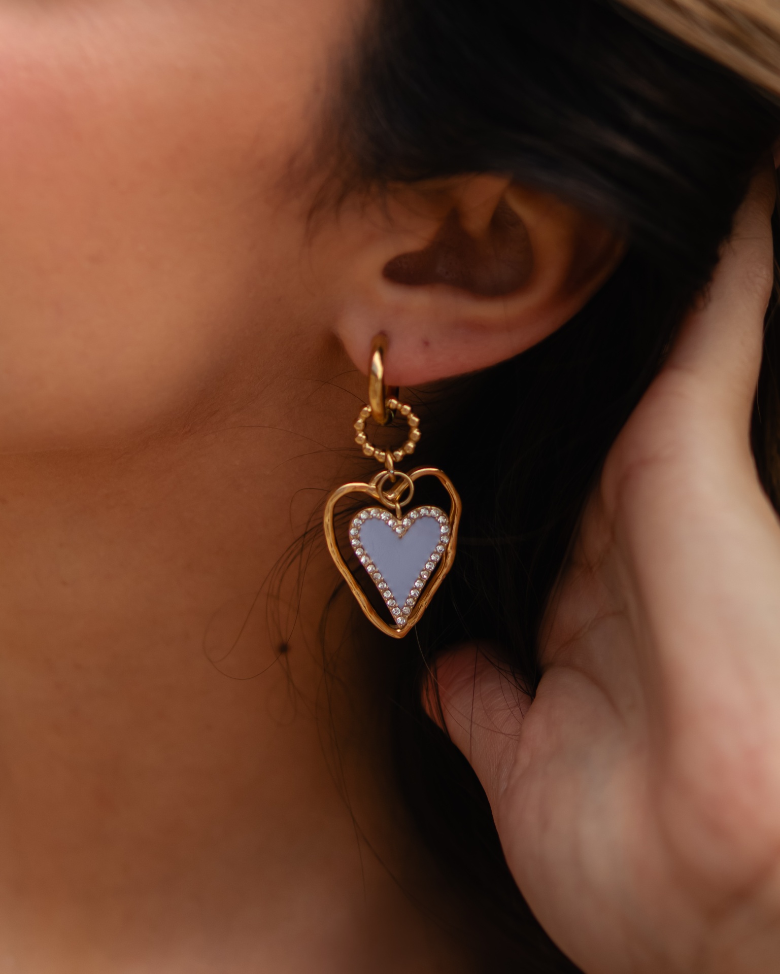 Brinco dourado com pingente de coração azul claro com cristais em orelha feminina