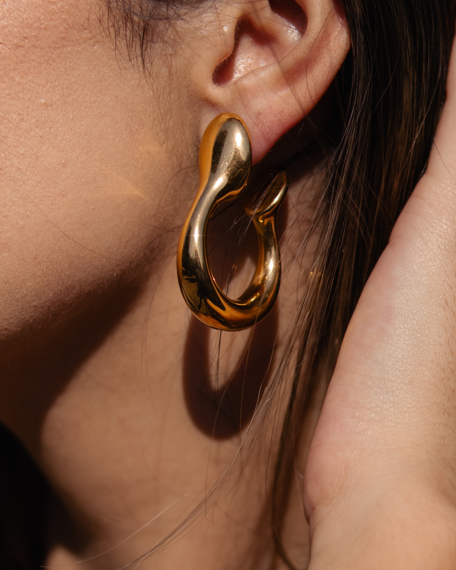 Brinco dourado pendente com design curvo na orelha de uma pessoa.