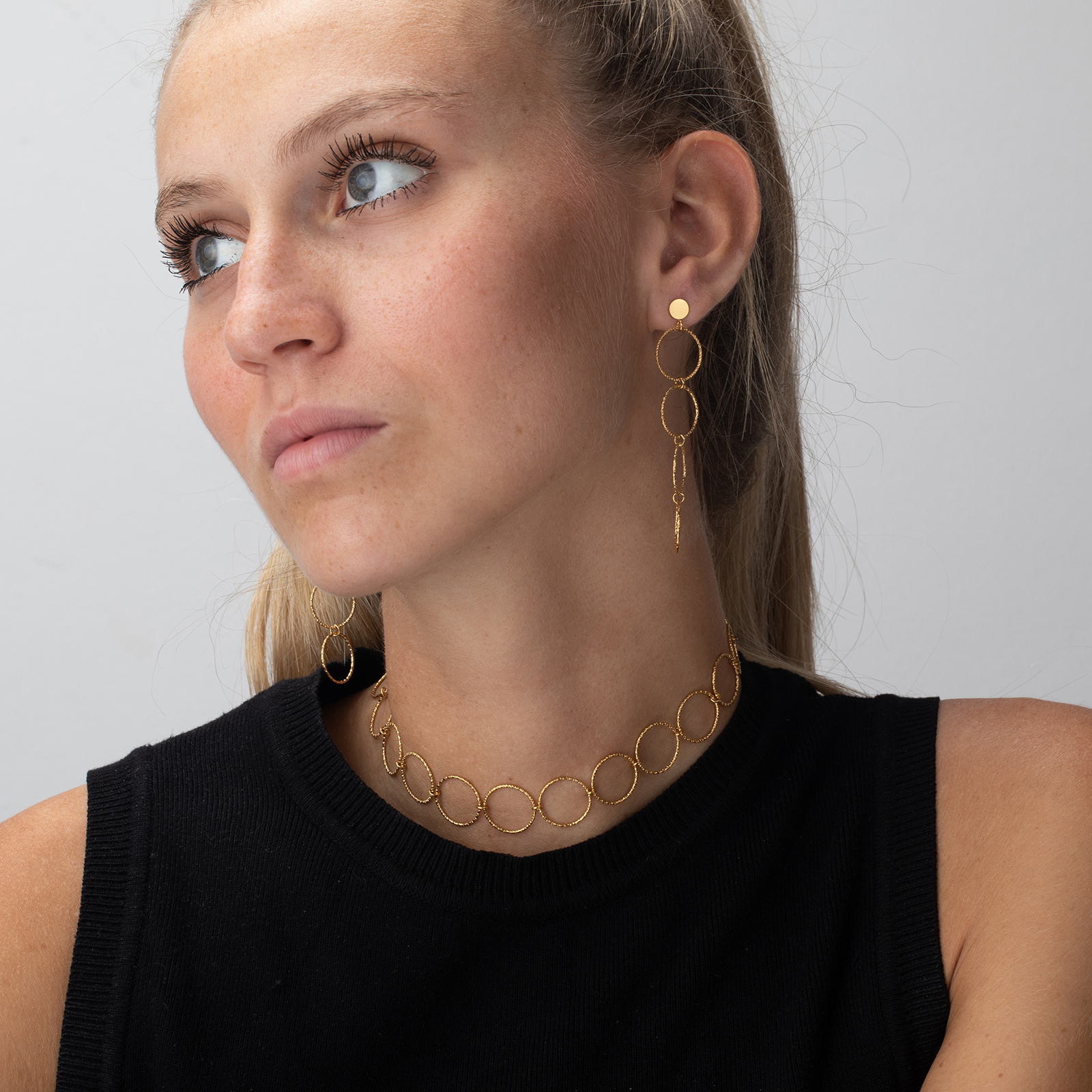 Mulher com brincos e colar dourados com círculos interligados