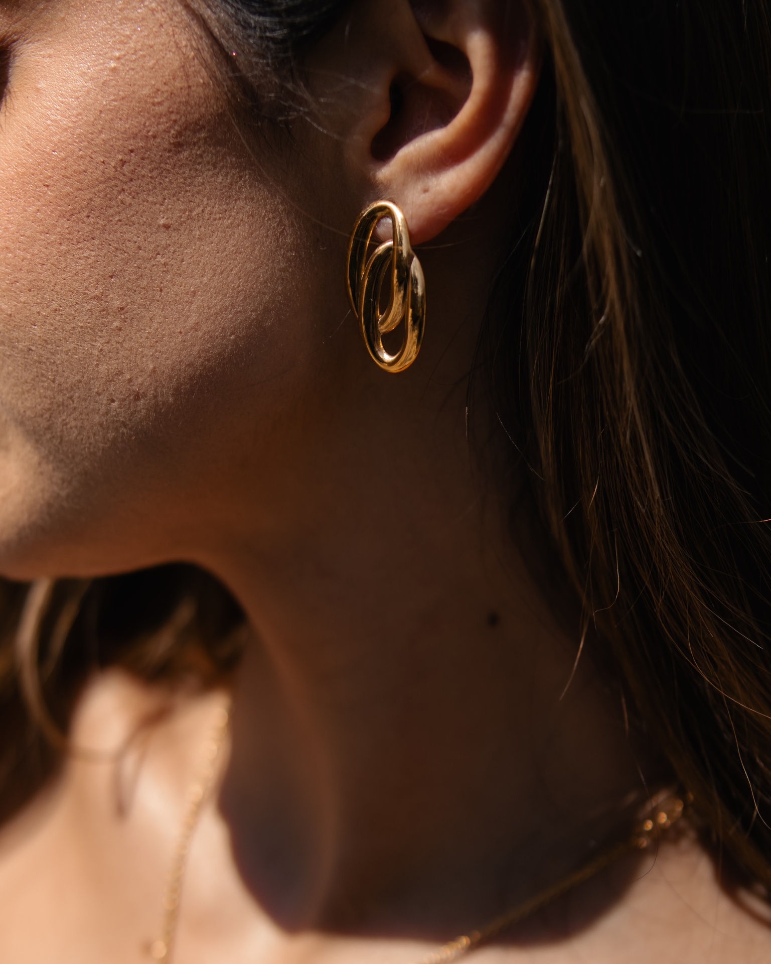 Brinco dourado em forma de elipse com design de aro duplo na orelha de uma mulher