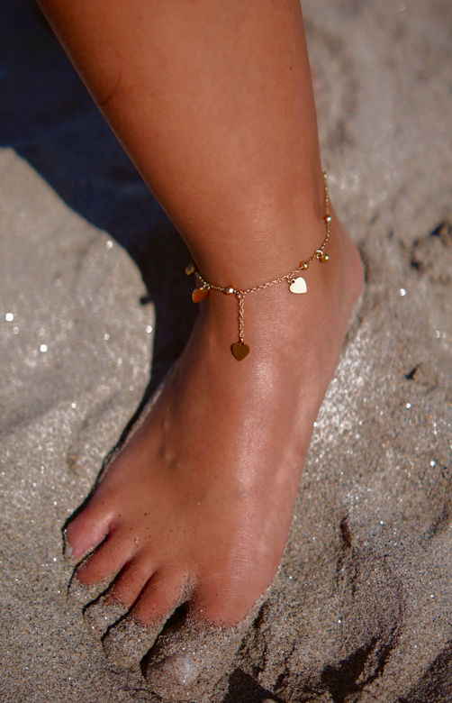 Tornozeleira dourada com pendentes de coração num pé na areia