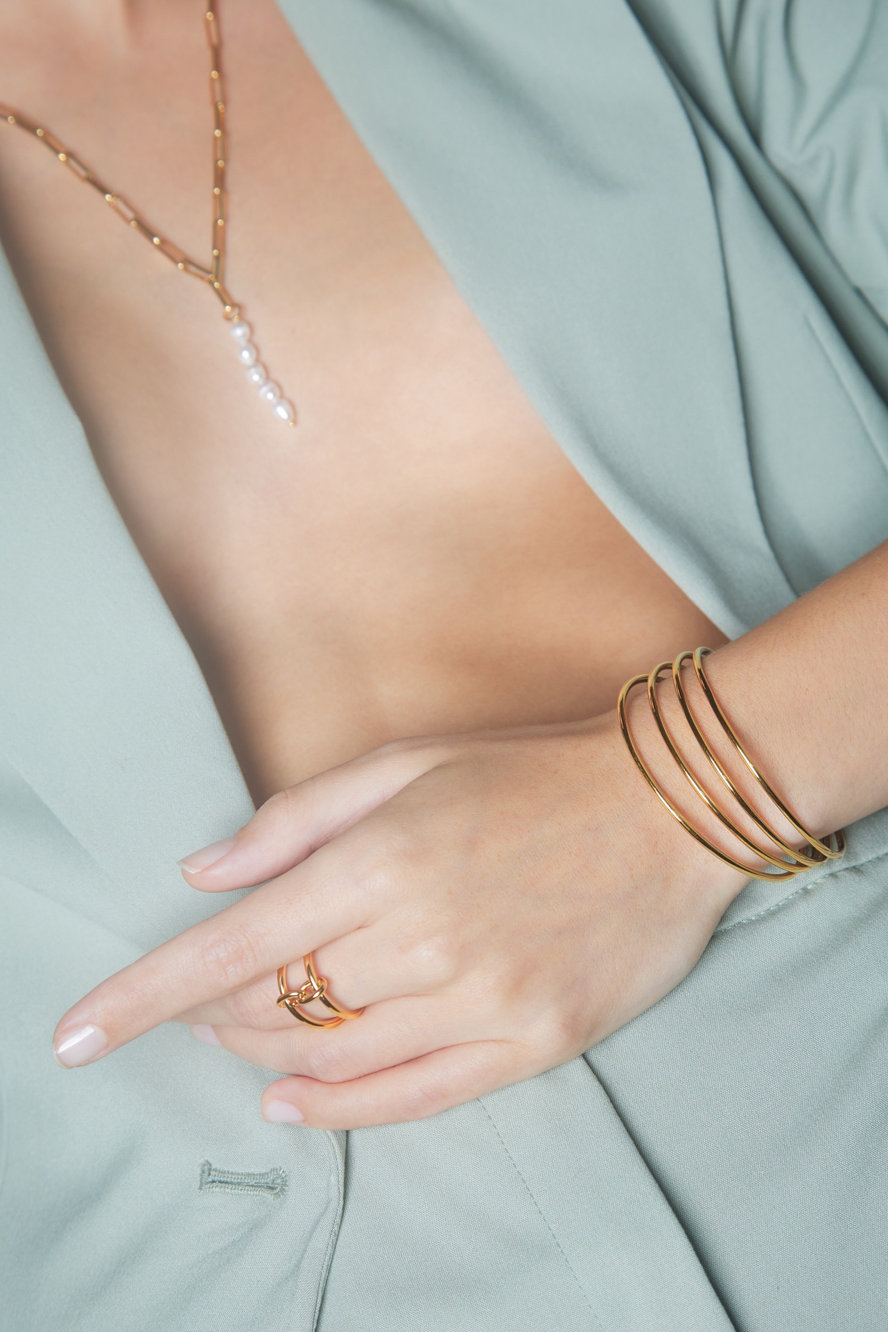 Colar, anel e pulseiras dourados usados por pessoa com roupa verde água