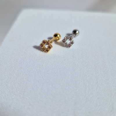 Dois piercings metálicos em dourado e prateado com pedras brilhantes sobre superfície branca