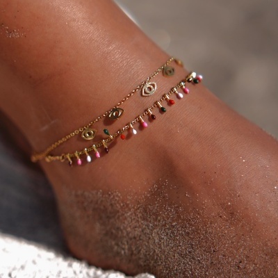 Duas tornozeleiras douradas delicadas com pendentes coloridos e amuletos em tornozelo arenoso na praia