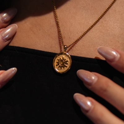 Colar dourado com pendente em forma de sol e unhas compridas nude