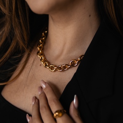 Colar e anéis dourados de elos grossos numa mulher com casaco preto