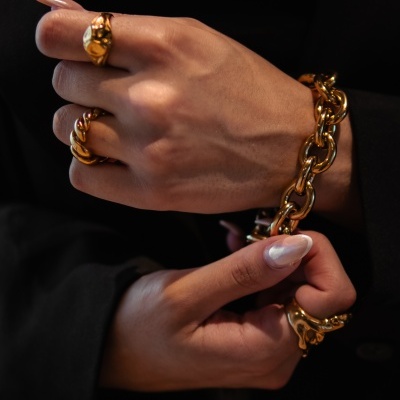 Mãos femininas com acessórios dourados e unhas brancas em fundo preto