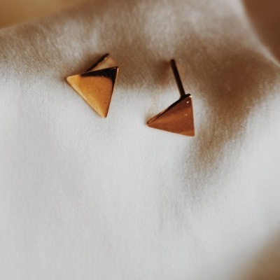 Brincos triangulares dourados sobre tecido branco