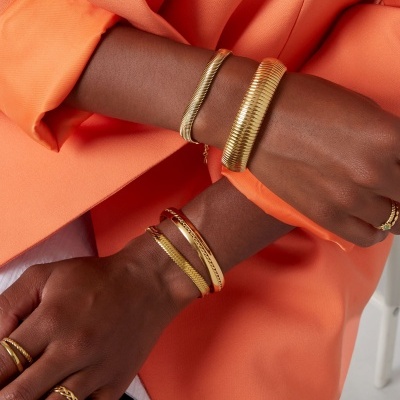 Pulseiras e anéis dourados em braços com casaco laranja