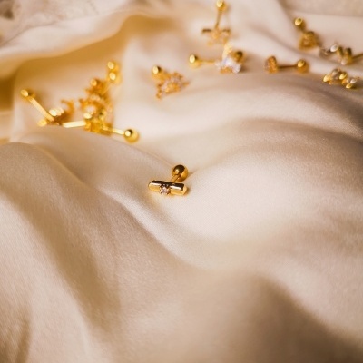 Brincos dourados sobre tecido branco acetinado e renda