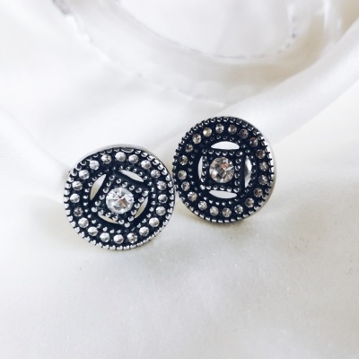 Brincos redondos pretos com detalhes prateados e pedra central sobre tecido branco