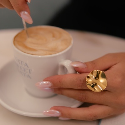 Mão com anel dourado a segurar caneca branca com sopa cremosa
