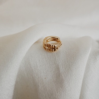 Anel dourado com padrão de cortes verticais sobre tecido branco.