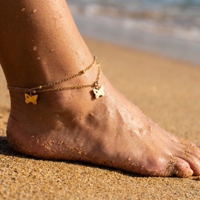 Pé com tornozeleira dourada na praia com areia e água