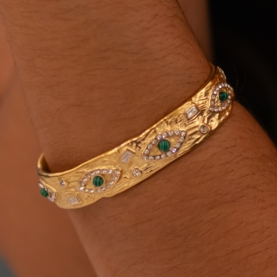 Pulseira dourada com pedras verdes num pulso