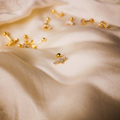 Vários brincos dourados com pedras sobre tecido branco de seda com bordado