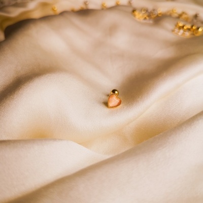 Brinco dourado com coração cor-de-rosa sobre tecido branco acetinado