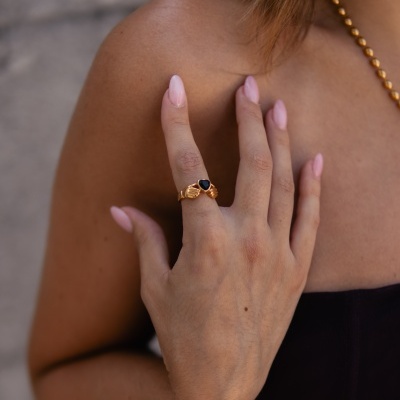 Anel dourado com pedra preta em forma de coração na mão de uma mulher