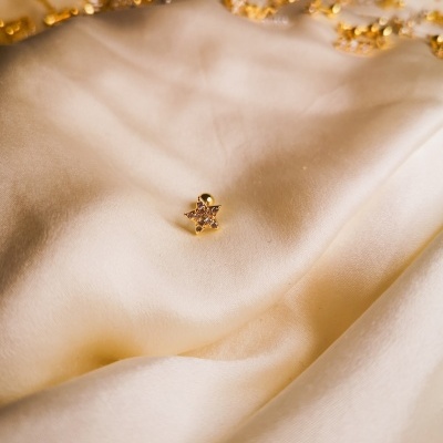 Brinco em forma de estrela sobre tecido creme com franjas douradas ao fundo