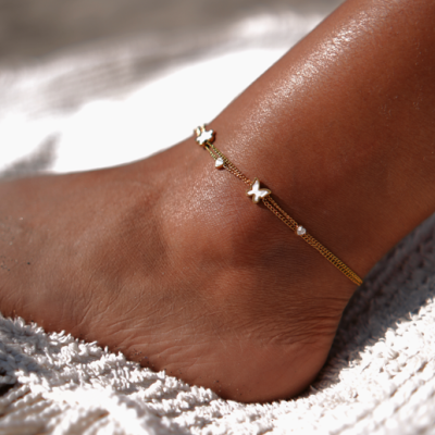 Tornozeleira dourada com borboletas no tornozelo sobre manta branca