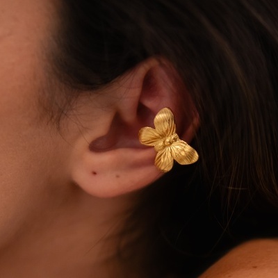 Brinco dourado em forma de borboleta na orelha de uma pessoa