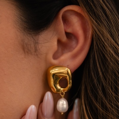 Brinco dourado com pérola pendente numa orelha feminina