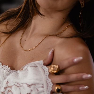 Colar dourado fino, anéis dourados e roupa branca rendada em modelo