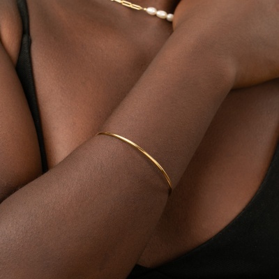 Pulseira dourada fina num braço com colar de pérolas e roupa preta