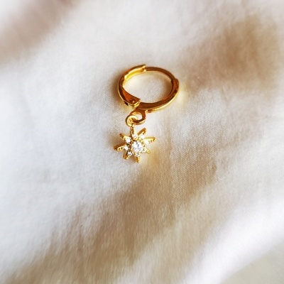 Brinco dourado com pendente floco de neve sobre tecido branco