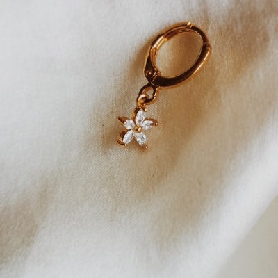 Brinco dourado com pendente de flor e pedras brancas sobre tecido branco