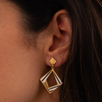 Brinco dourado geométrico com detalhes coloridos usado numa orelha