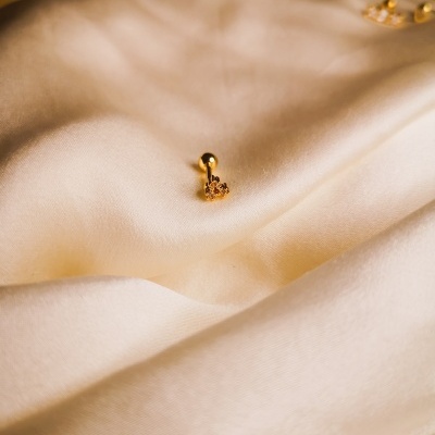 Brinco dourado pequeno em tecido branco com outros brincos ao fundo
