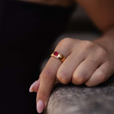 Anel dourado com pedra vermelha em mão sobre superfície de pedra