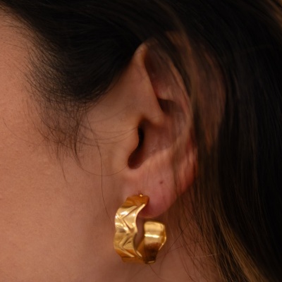 Brinco dourado de argola com textura irregular na orelha