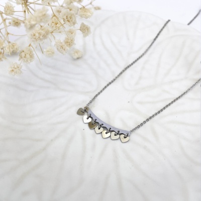 Colar em aço com pendentes de coração sobre prato branco com flores secas