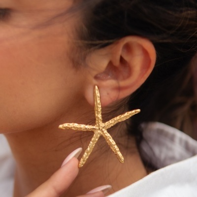 Brinco dourado em forma de estrela do mar na orelha de uma mulher