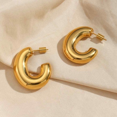 Brincos dourados em forma de argola sobre tecido bege