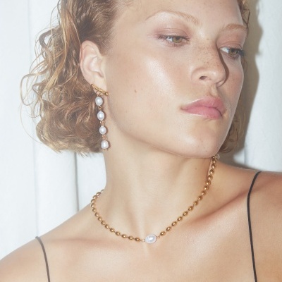 Colar e brinco de pérolas em dourado usados por mulher com top preto.