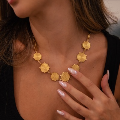 Colar dourado com elementos hexagonais texturizados no pescoço de uma mulher