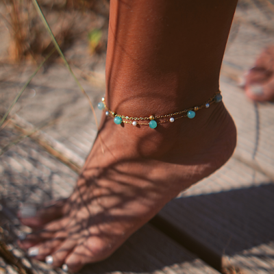 Tornozeleira dourada com contas azuis e pérolas num pé bronzeado