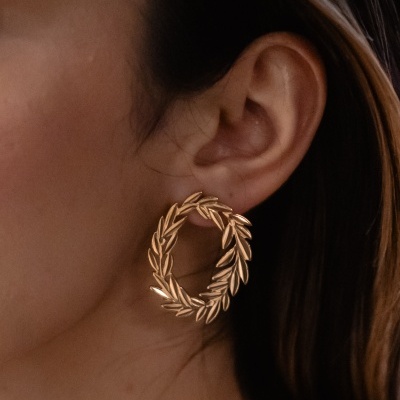 Brinco dourado circular com folhas na orelha
