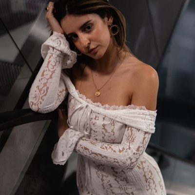 Mulher com vestido branco de renda ombro a ombro em ambiente interior moderno