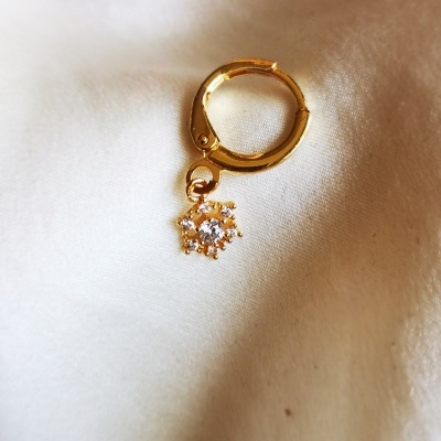 Brinco dourado com pendente em forma de estrela sobre tecido branco