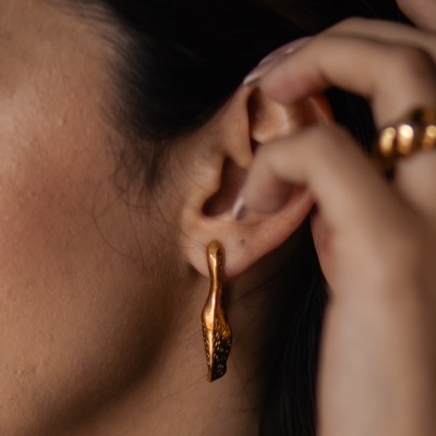 Brinco dourado em orelha de mulher com textura irregular