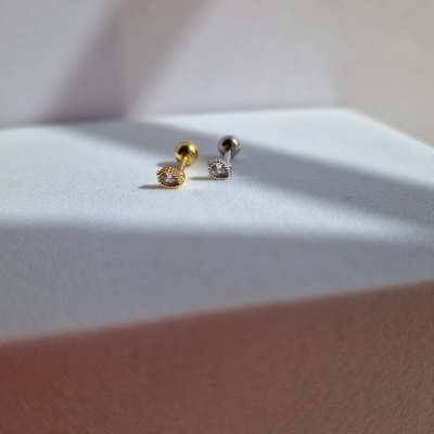 Dois brincos pequenos, um dourado e um prateado, sobre superfície branca