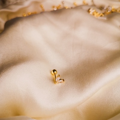 brinco dourado com pedra sobre tecido bege claro acetinado