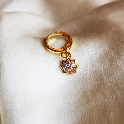 Brinco dourado com pendente de flor e pedras sobre tecido branco